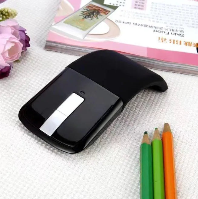 Black folding Bluetooth wireless mouse shown both folded and unfolded beside laptop
