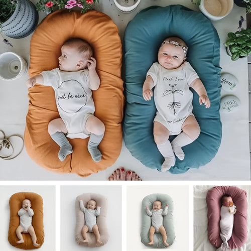 Cotton portable baby nest crib for newborns, beige colour, shown on a bed.