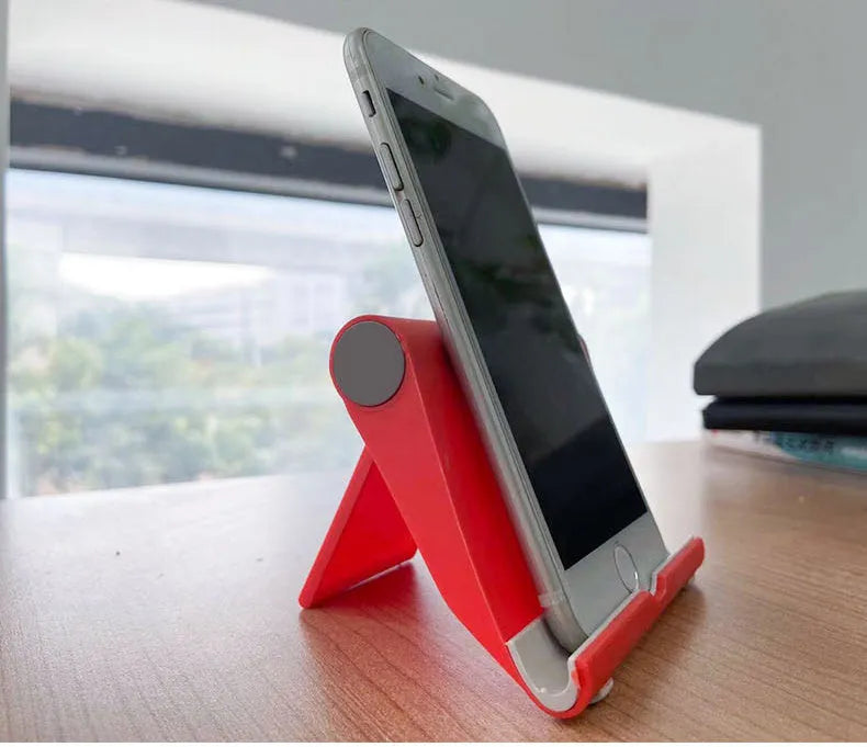 Black PE folding stand holding a smartphone at an angle on a wooden table.