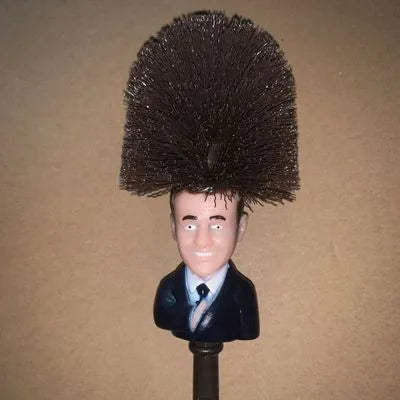 Yellow plastic Donald Trump toilet brush with hanging slot on handle.