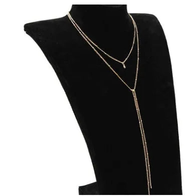 Multilayer lariat necklace in gold with three alloy chains on a plain background