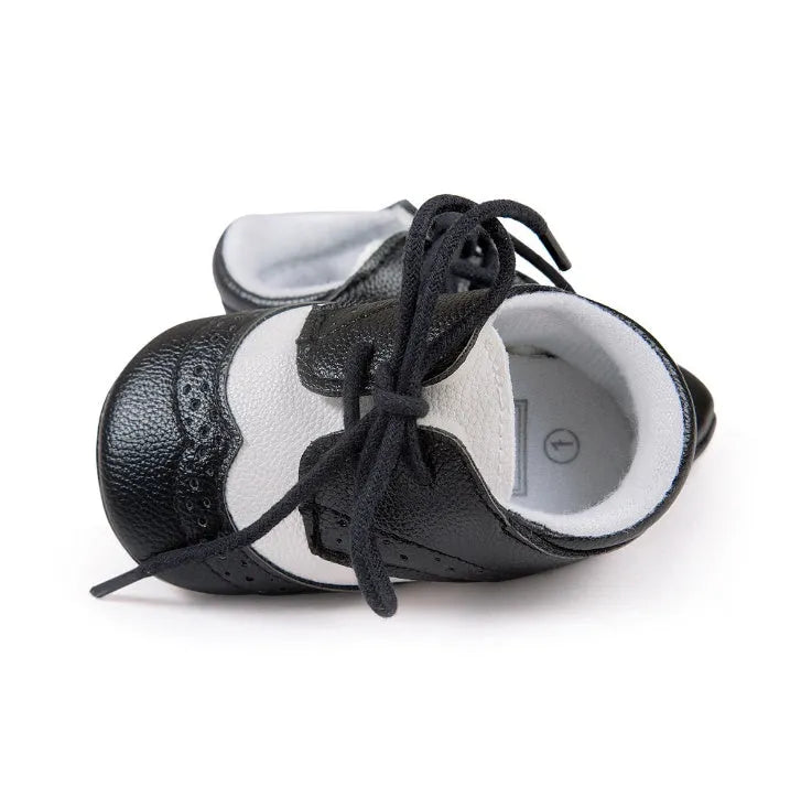 Vintage-style soft-soled baby shoes in black, grey, light brown, and white for infants 0-12 months.