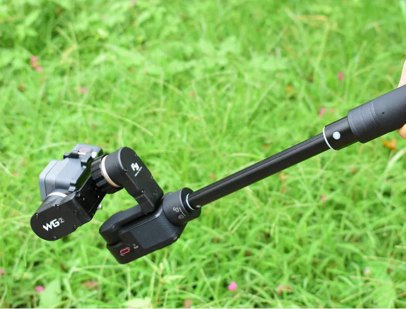 Black retractable aluminium selfie stick extended with phone attached, showing Bluetooth remote and tripod stand.