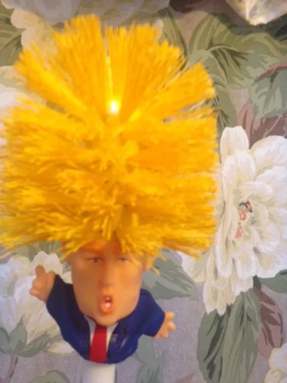 Yellow plastic Donald Trump toilet brush with hanging slot on handle.