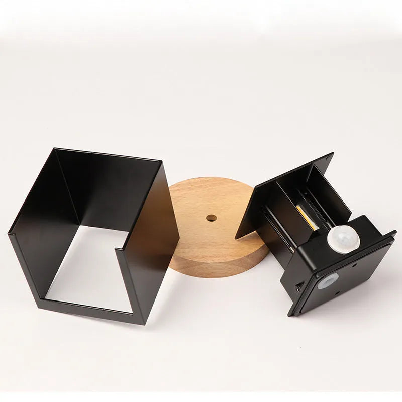Square aluminium wall lamp in black on a corridor wall, showing adjustable colour temperature settings from warm to cool light.