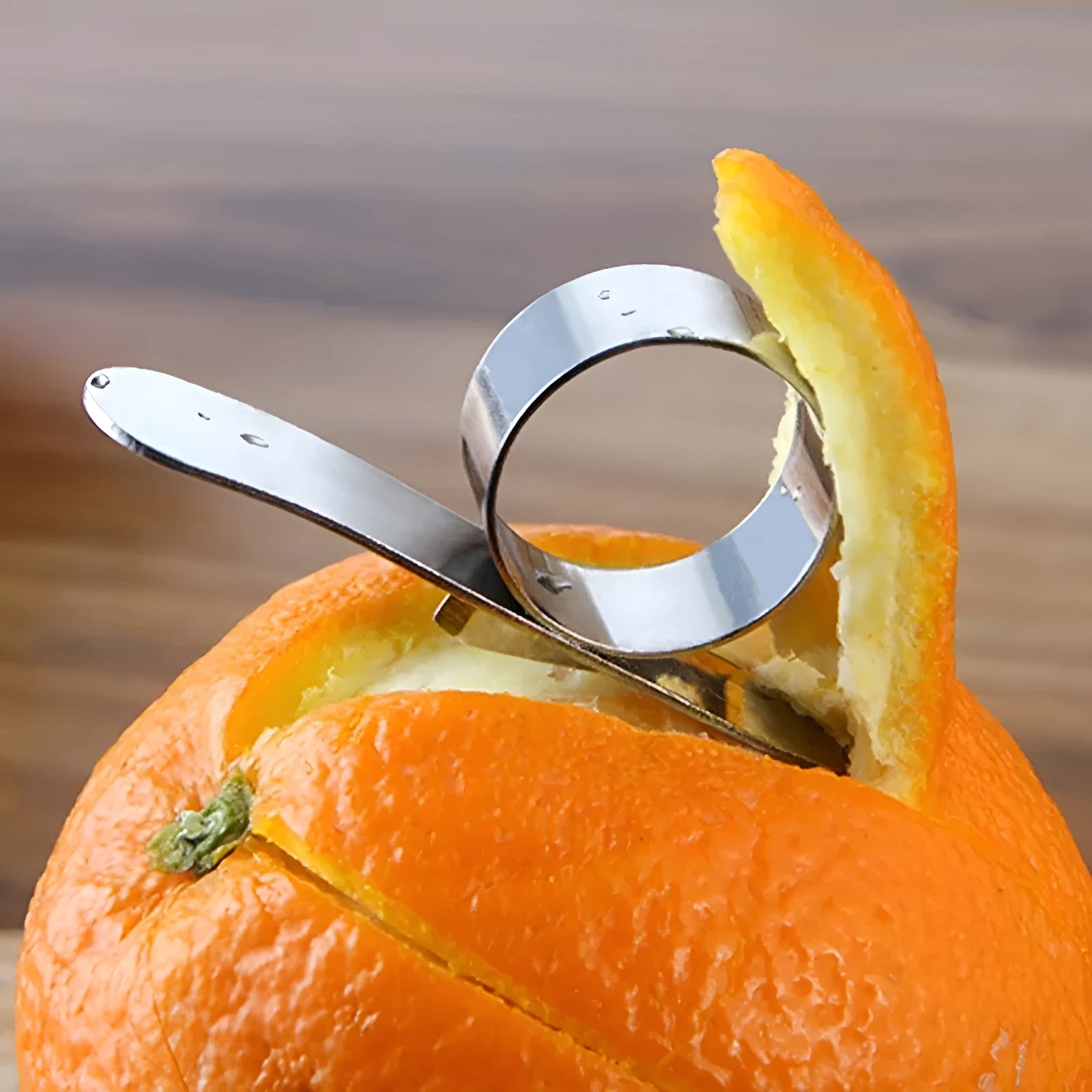 Silver stainless steel citrus fruit peeler with a ring-shaped handle on a kitchen surface.