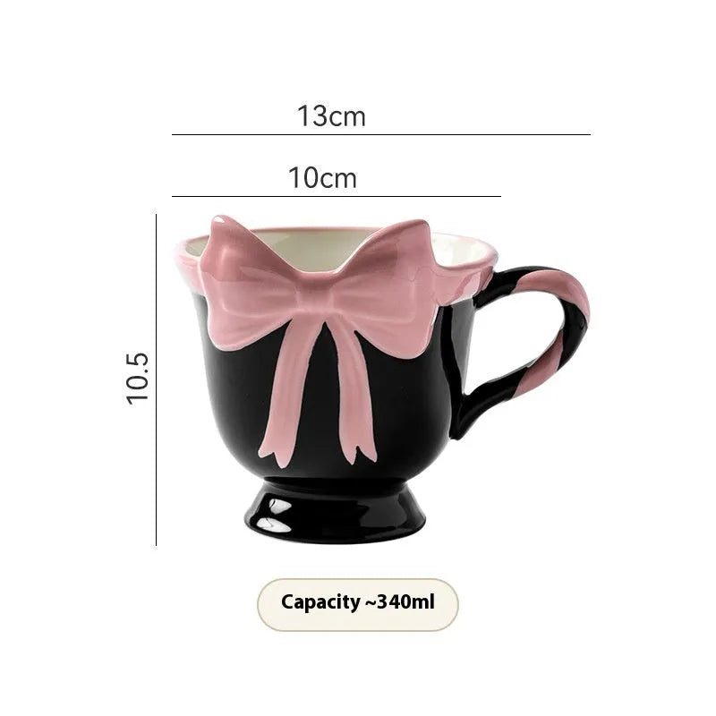 Cute white ceramic mug with a pink heart and black bow design, showing its handle.