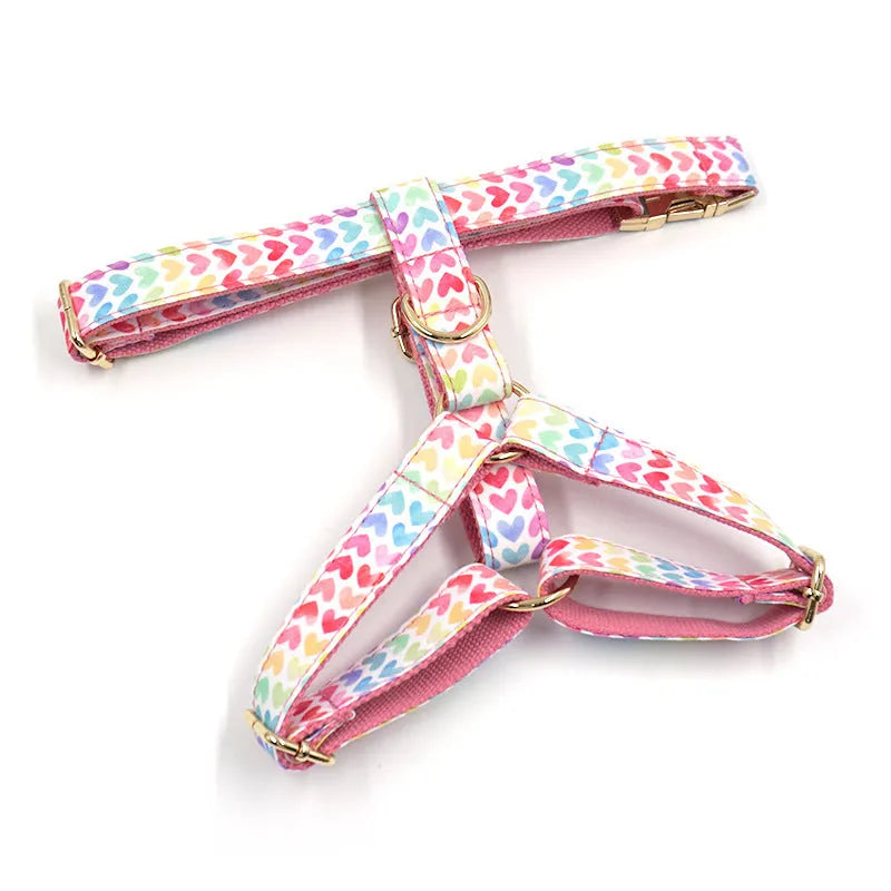 Pink dog harness with a gold buckle and colourful heart-shaped stone decoration on an adjustable polyester strap.
