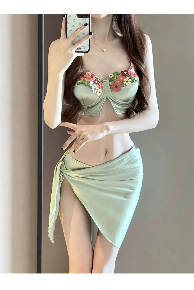 Green women's three-piece bikini set with triangle top, briefs, and skirt on hanger