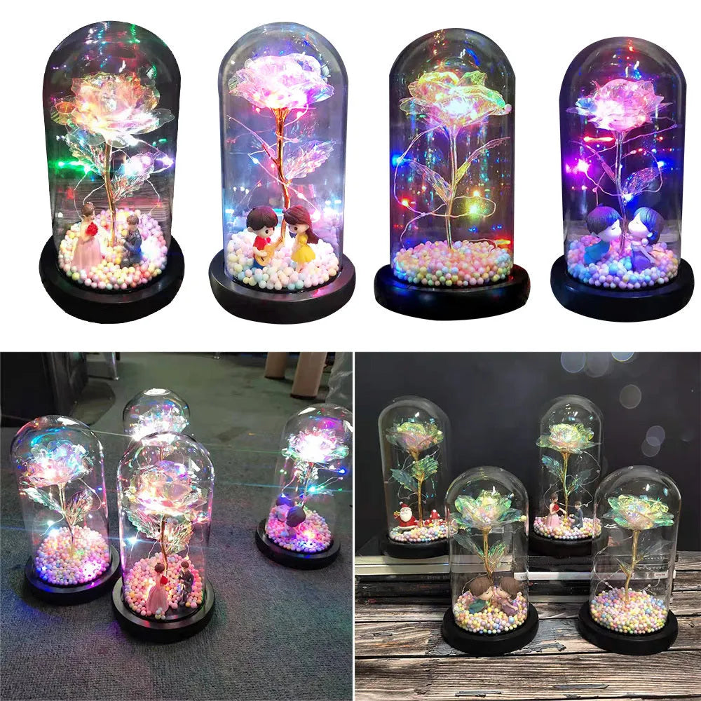 Artificial gold rose flower inside a glass lantern with LED lights and black base on a table.