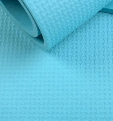 Red EVA fitness yoga mat with rolled edge showing thickness, laid flat on a wooden floor.