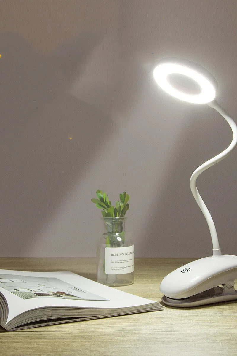 Modern clip-on rechargeable desk lamp with a white plastic shade and touch controls on its base.
