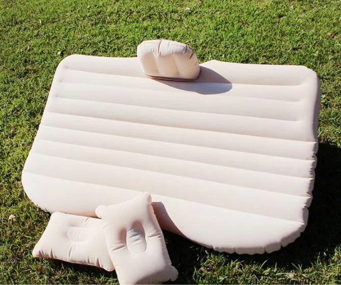 Black inflatable car bed with flocked surface, shown with storage bag and pillows, ready for use in a vehicle.