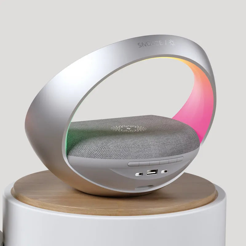 Beige multifunctional wireless charging clock with Bluetooth speaker and warm white LED wake-up light on a wooden table.