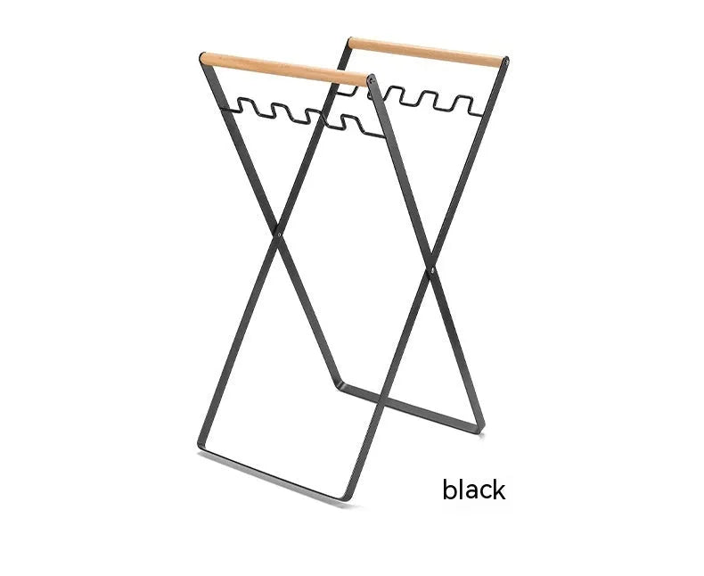 Black iron folding trash storage rack with a wooden handle for hanging bin bags.