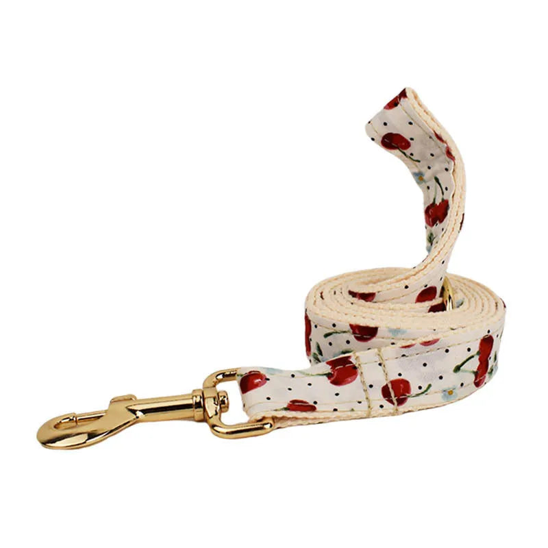 Red cherry print dog collar and leash set with light gold buckle, matching vest, bow, and poop bag holder.