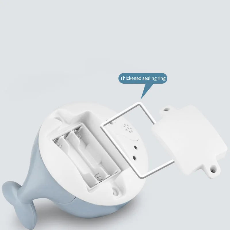 White and blue whale-shaped bath toy spraying water with LED lights on, floating in a baby bath