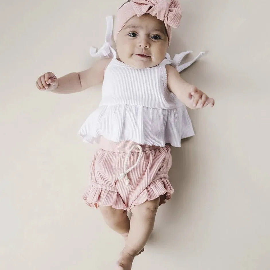 Baby girls white knitted cotton vest and pink shorts set on a light background