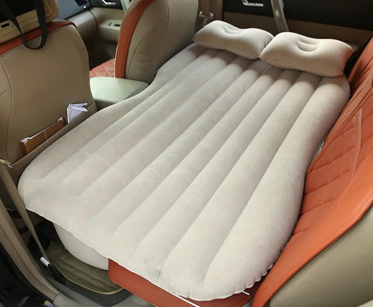 Black inflatable car bed with flocked surface, shown with storage bag and pillows, ready for use in a vehicle.