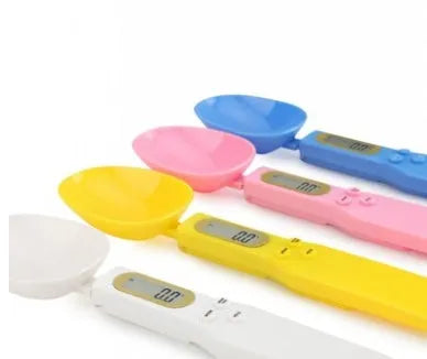 White digital kitchen scale with LCD screen displaying weight, shown next to a measuring spoon.