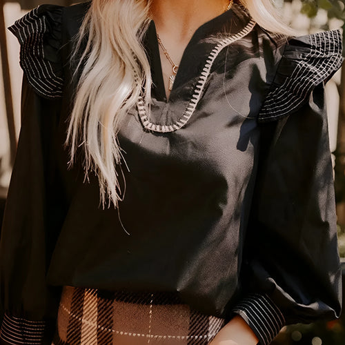 Black V-neck long sleeve blouse with ruffle trim and contrast stitching.