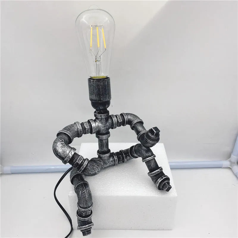 Custom industrial retro style iron pipe robot table lamp on a wooden desk.