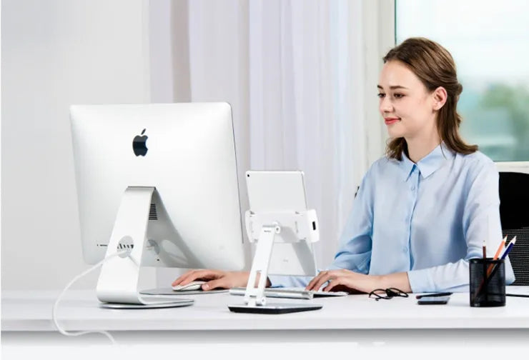 Silver foldable aluminium phone and tablet stand on a desk, holding a tablet at an angle.