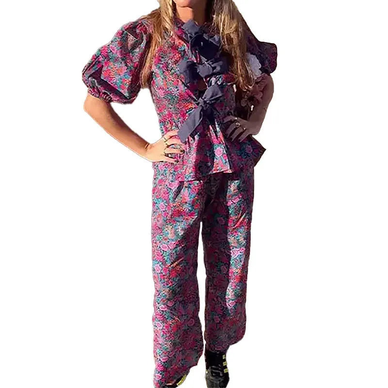 Women's floral print polyester trouser suit with tie-neck top and puff sleeves.