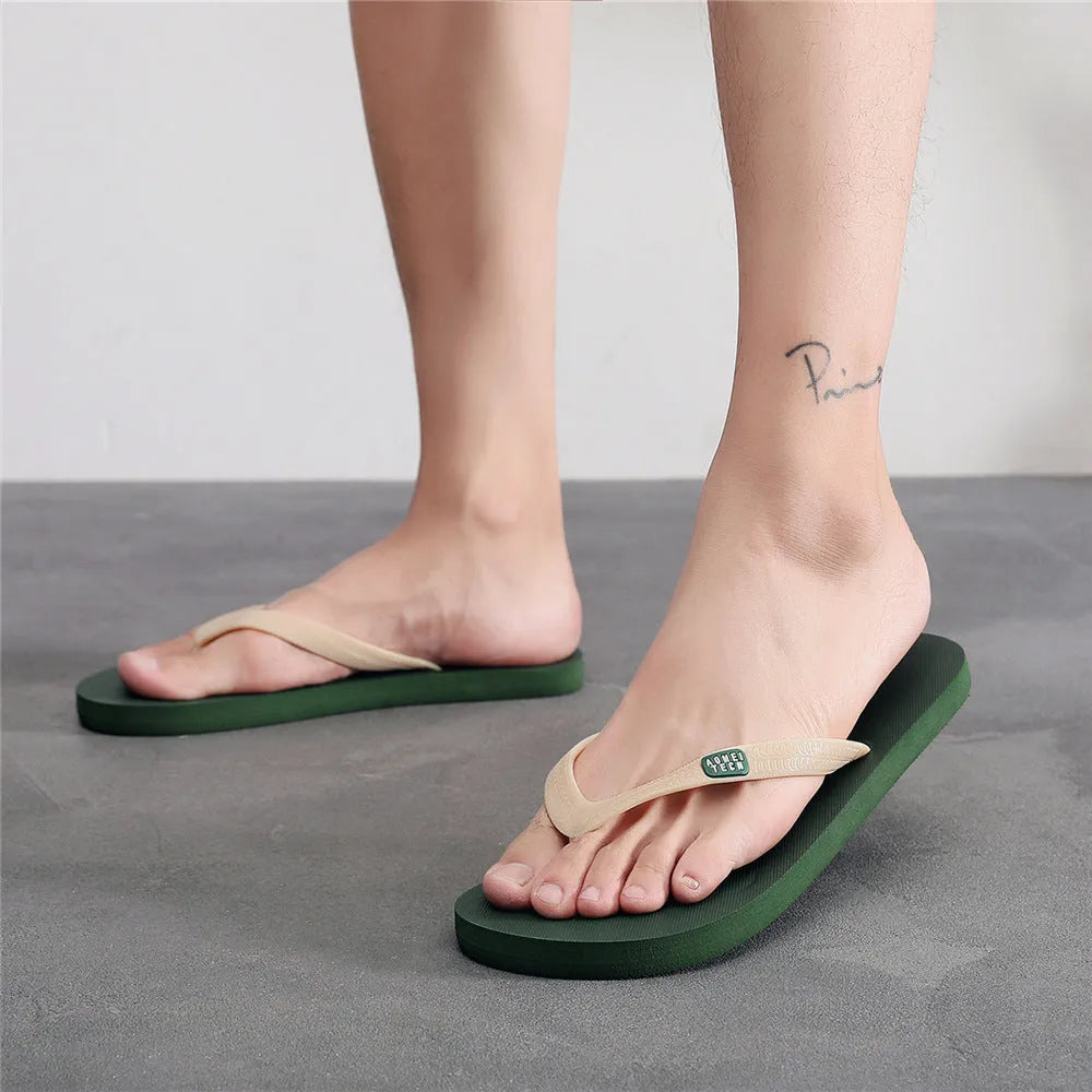 Men's black flip-flops with a textured rubber sole and EVA foam upper on a sandy beach.