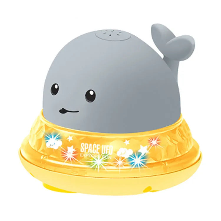 White and blue whale-shaped bath toy spraying water with LED lights on, floating in a baby bath