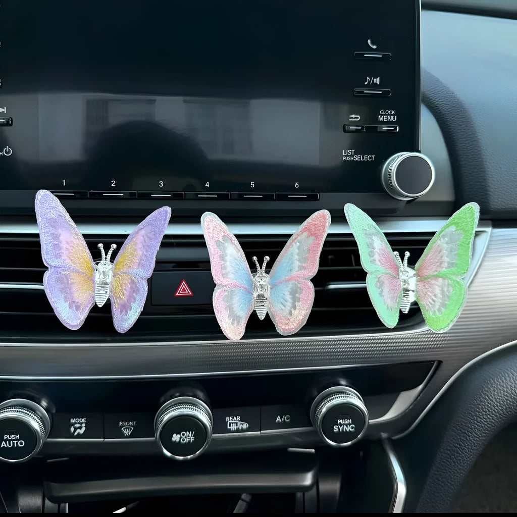 Fabric embroidered butterfly car air vent decoration in multiple colour options on a dashboard.