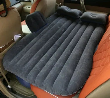 Black inflatable car bed with flocked surface, shown with storage bag and pillows, ready for use in a vehicle.