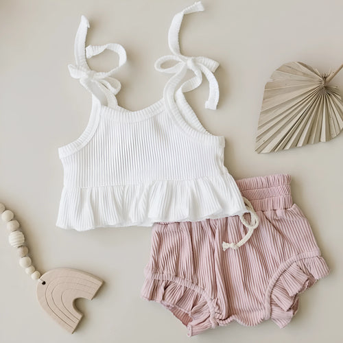 Baby girls white knitted cotton vest and pink shorts set on a light background