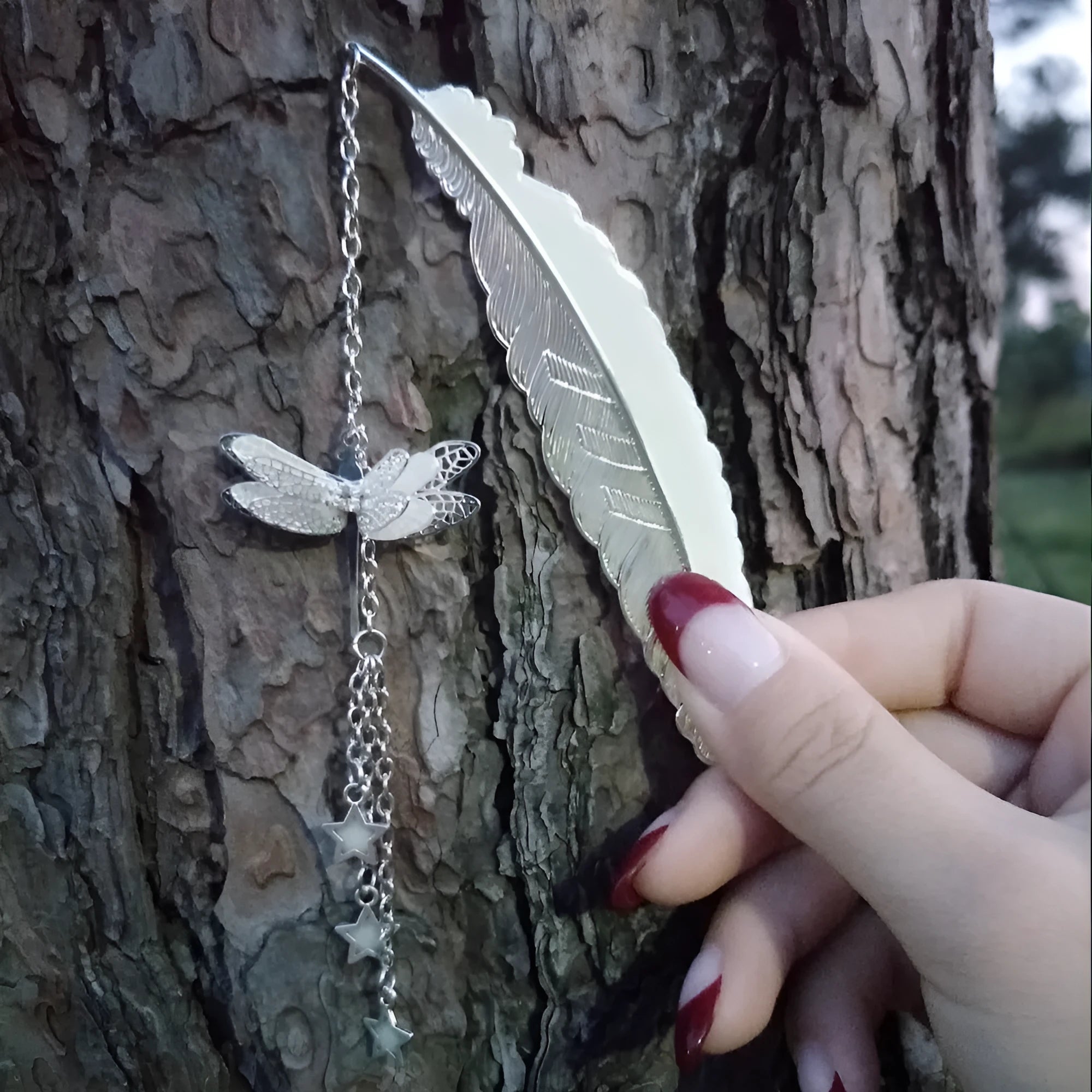 Silver pure copper feather bookmark with glowing luminous butterfly charm on a book.
