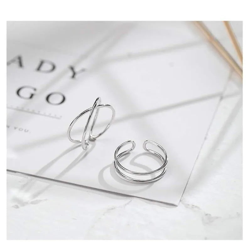 Silver plated geometric cross ring with adjustable opening on a plain background