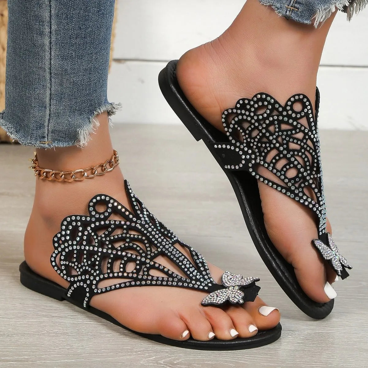Women's black slip-on sandals with rhinestone details and flip-toe design on a flat rubber sole