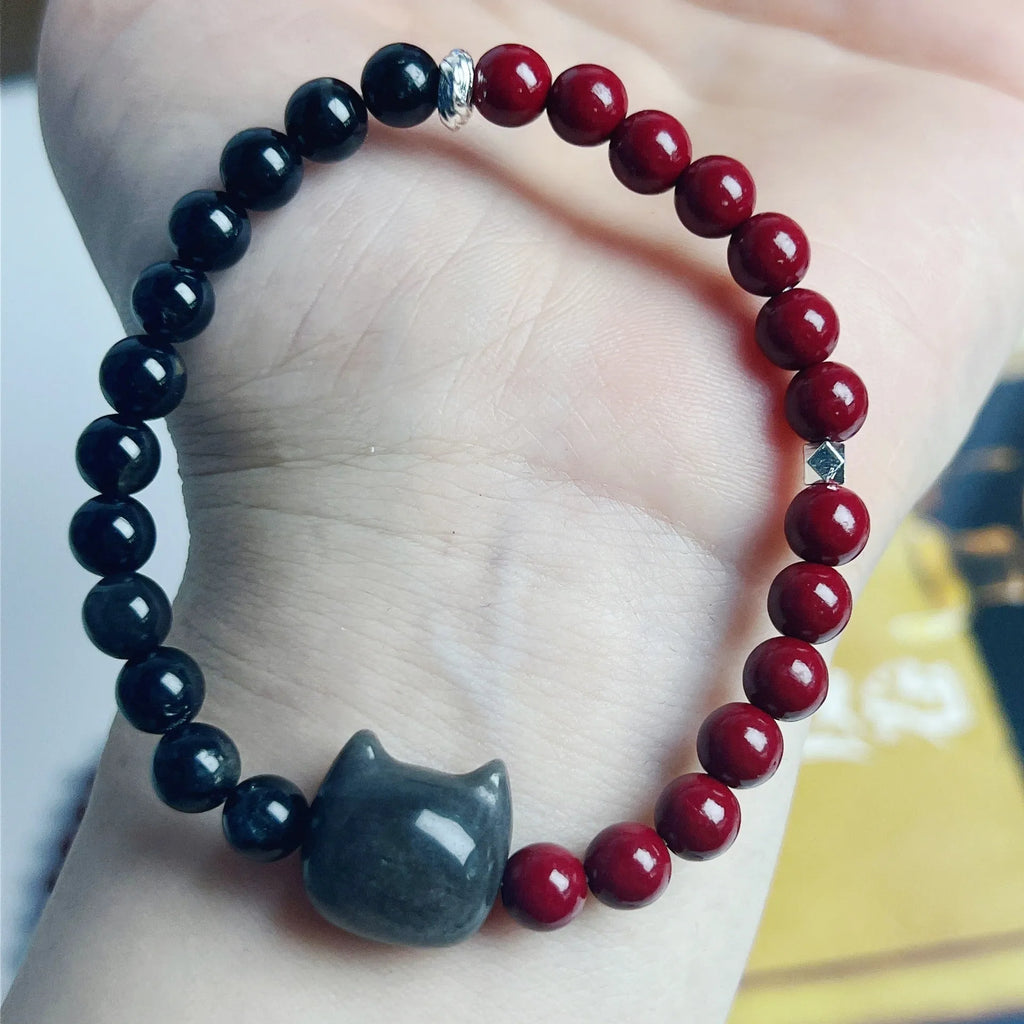 Black obsidian cat bracelet with golden crown charm and red bead on elastic cord
