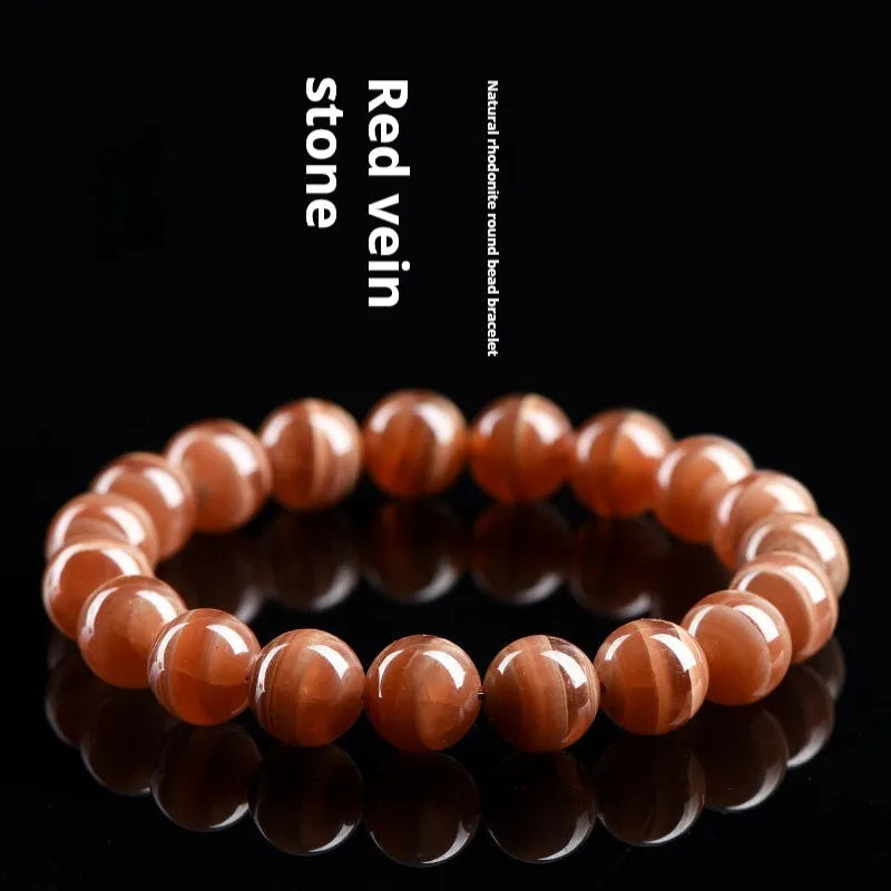Natural old mine rhodochrosite round bead bracelet with Ruyi detail on a wrist.