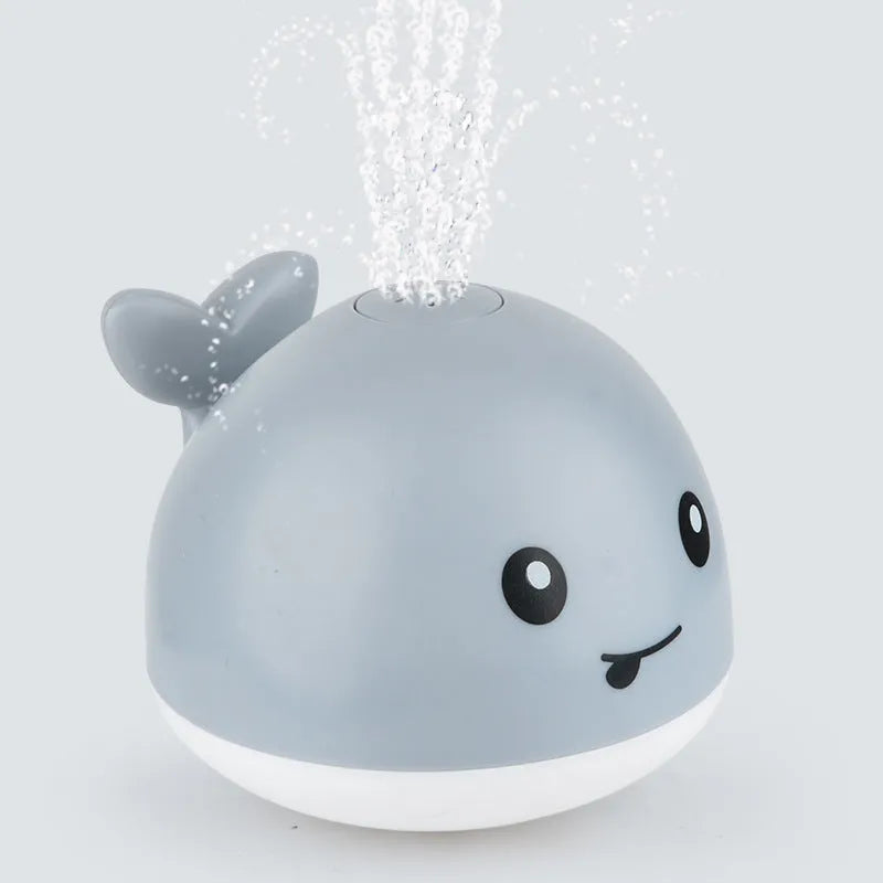 White and blue whale-shaped bath toy spraying water with LED lights on, floating in a baby bath