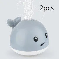 White and blue whale-shaped bath toy spraying water with LED lights on, floating in a baby bath