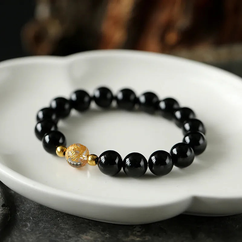 Geometric obsidian and white crystal bracelet with a golden dragon focal bead on a wrist.