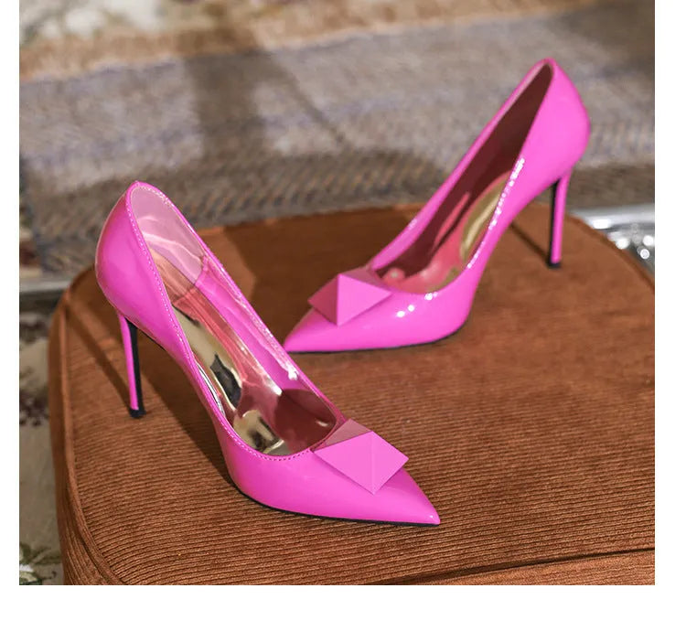 Pink patent leather women's stiletto heels with pointed toe, rivet decor, and a buckle.