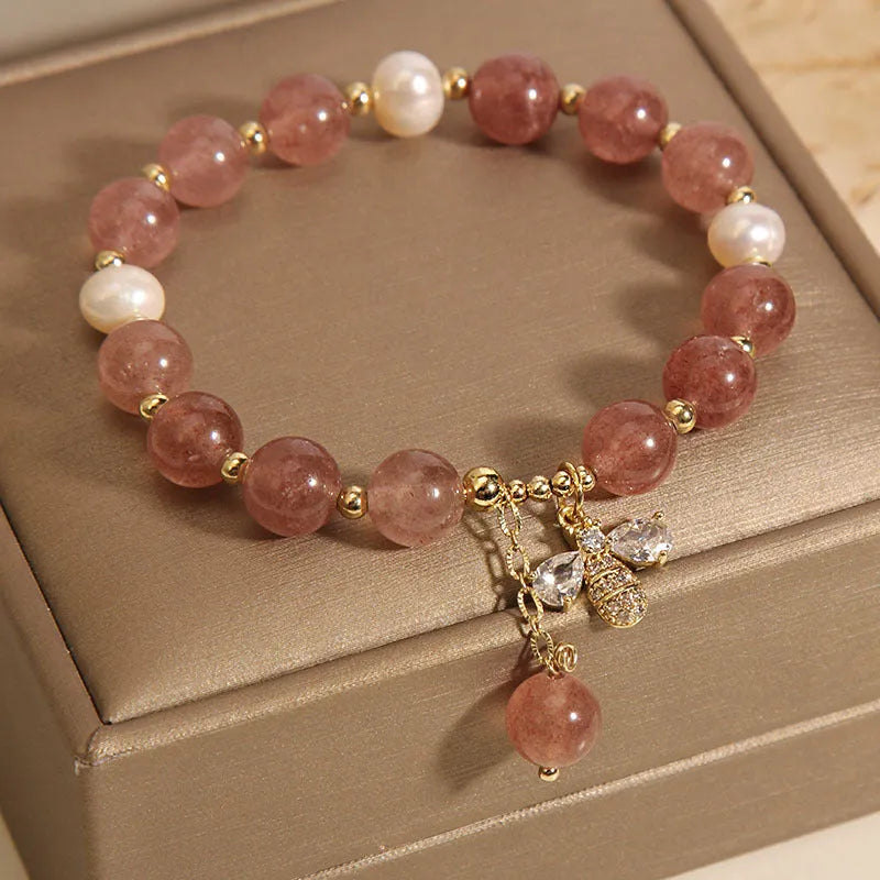 Adjustable pink strawberry quartz bracelet with three freshwater pearls and sparkling zircon charms on a wrist.