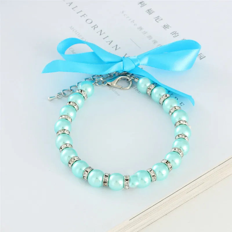Small dog wearing adjustable diamond pearl necklace with rhinestones and ribbon bow in blue colour
