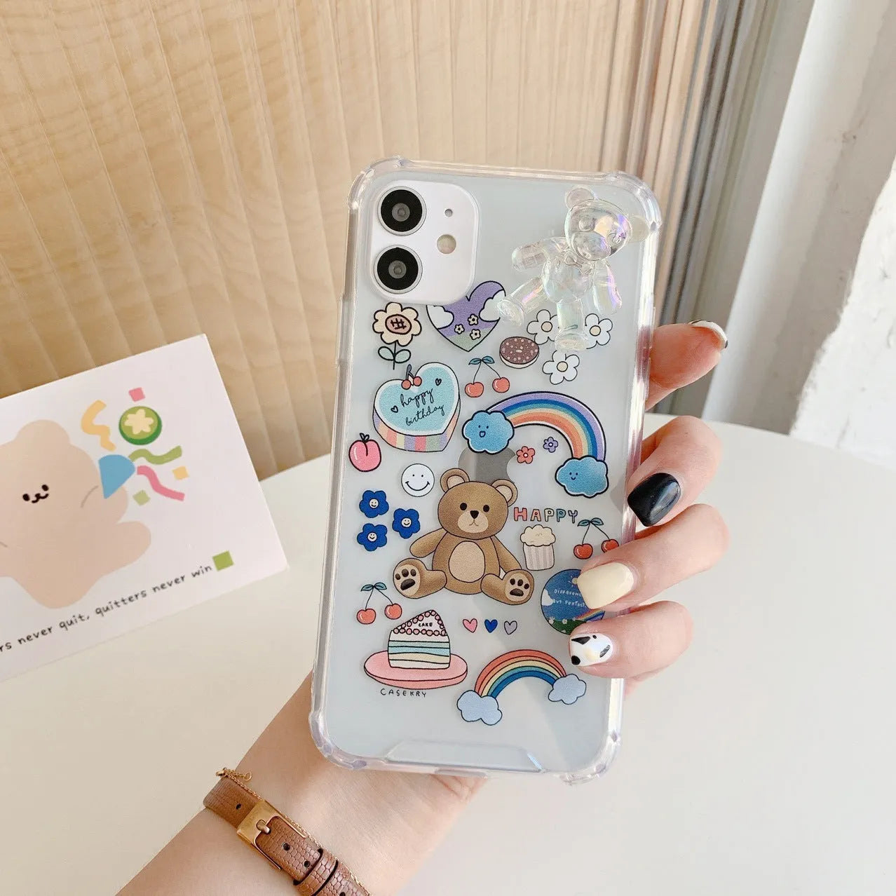 White iPhone case with a bear cartoon design and a silver chain with a bear pendant attached.