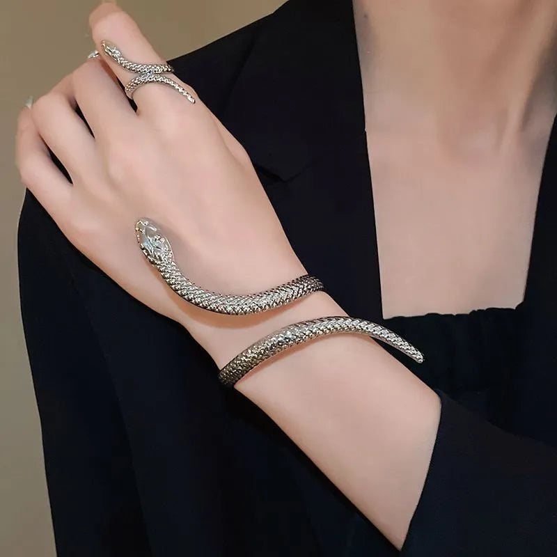 Gold exaggerated twisted snake design bracelet and ring jewellery set on a dark background.