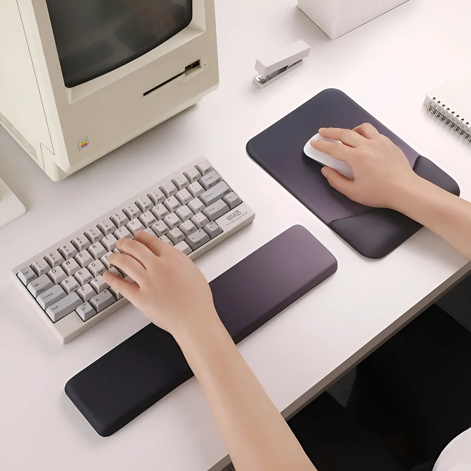 Square black silica gel wrist rest mouse pad on a desk, showing cloth surface and raised support pillow.