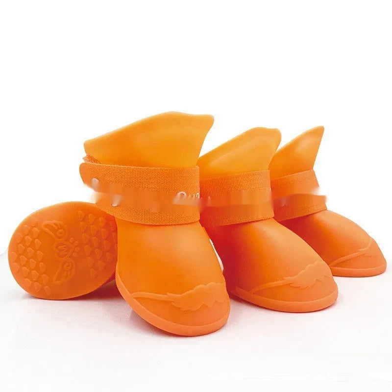 Set of four soft-soled rubber pet rain shoes in assorted colours on a grey background.