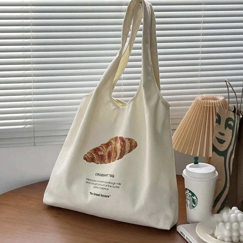 Beige canvas tote bag with bread print design showing adjustable shoulder strap and structured base