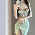 Green women's three-piece bikini set with triangle top, briefs, and skirt on hanger